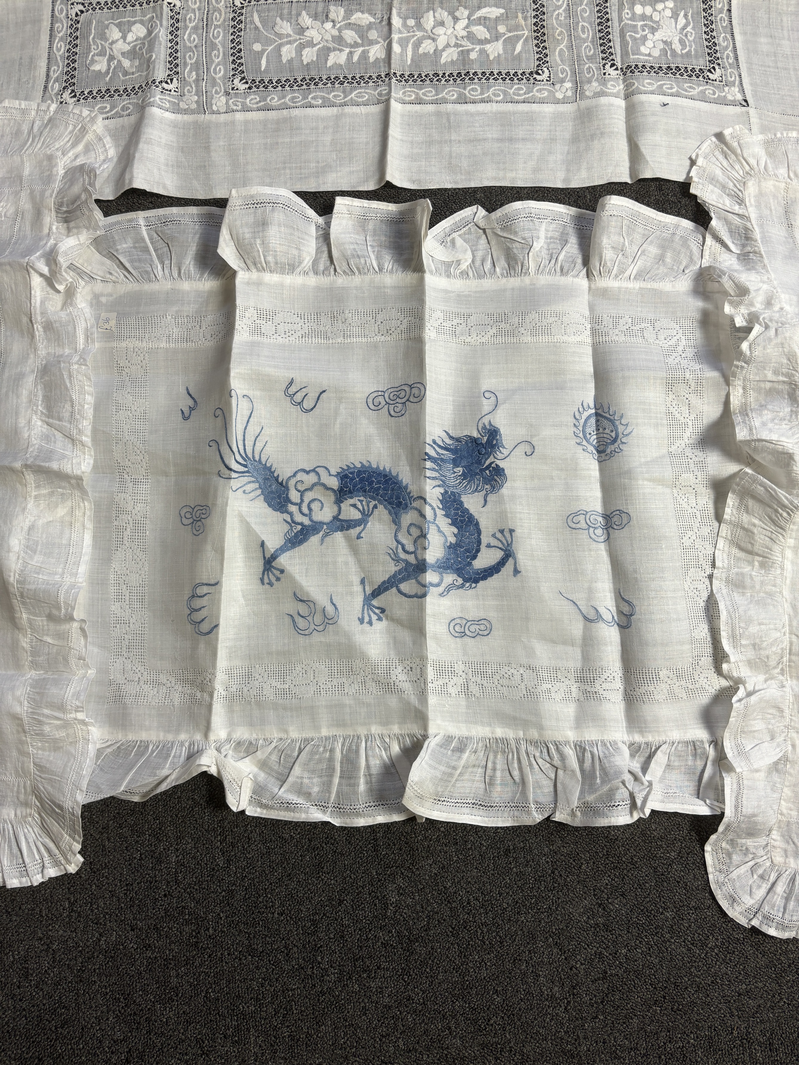 Chinese dragon and floral embroidered linen comprising two Chinese hand embroidered table cloths, both embroidered with blue dragons and flowers, together with a similar embroidered pillow case, a smaller cloth with whit